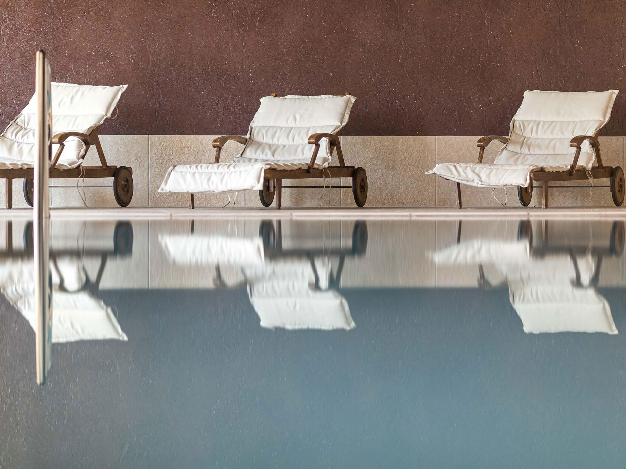 Three loungers by the indoor pool with white cushions - Hotel Patriarch