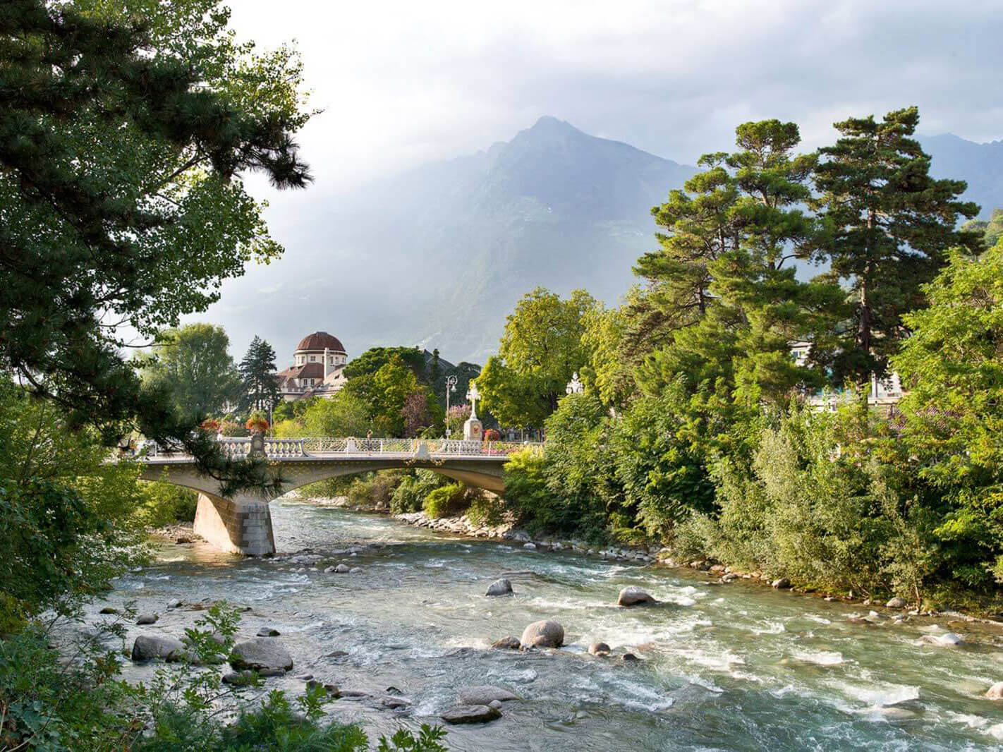 Eine Brücke über die Passer in Meran, davor die Flussufer - Hotel Patriarch