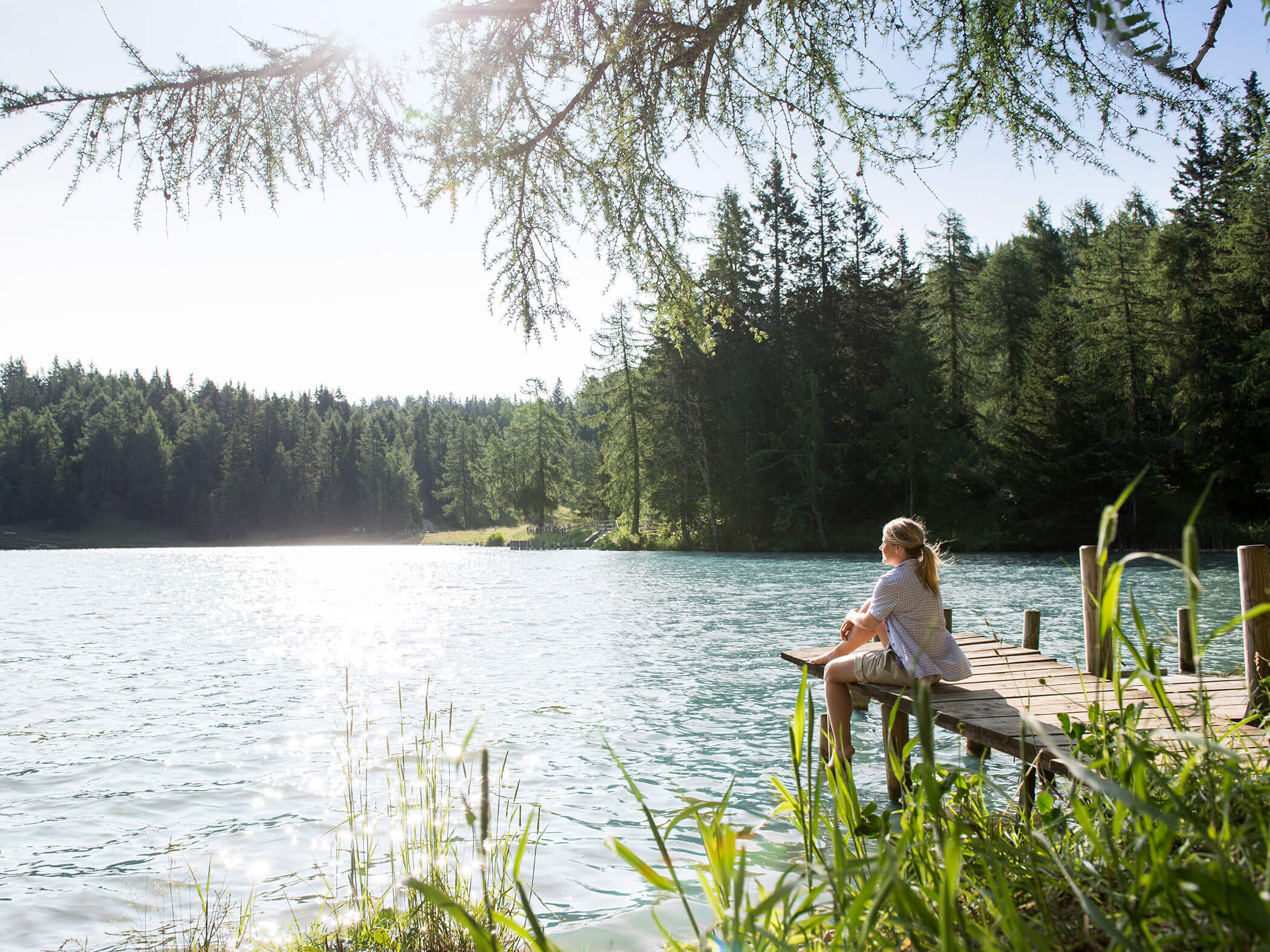 Eine Frau sitzt auf einem Steg im Sommer und blickt in das Wasser vom See - Hotel Patriarch