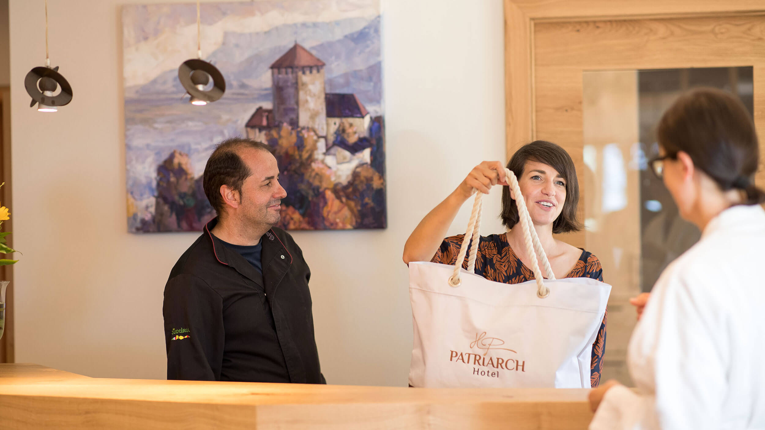 Die Rezeptionistin überreicht eine Wellnesstasche mit Handtüchern, Bademänteln etc. - Hotel Patriarch